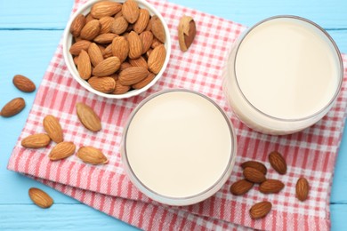 Photo of Fresh nut milk in glasses and almonds on light blue wooden table, flat lay