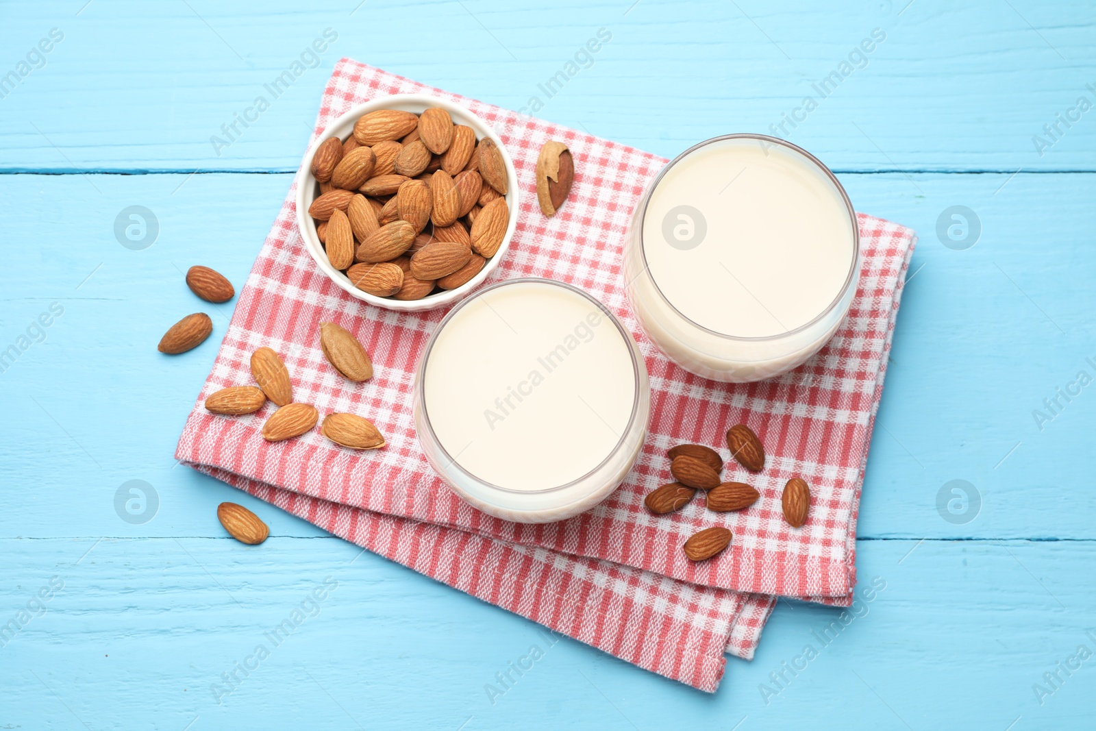 Photo of Fresh nut milk in glasses and almonds on light blue wooden table, flat lay