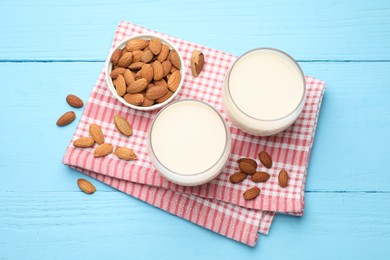 Fresh nut milk in glasses and almonds on light blue wooden table, flat lay