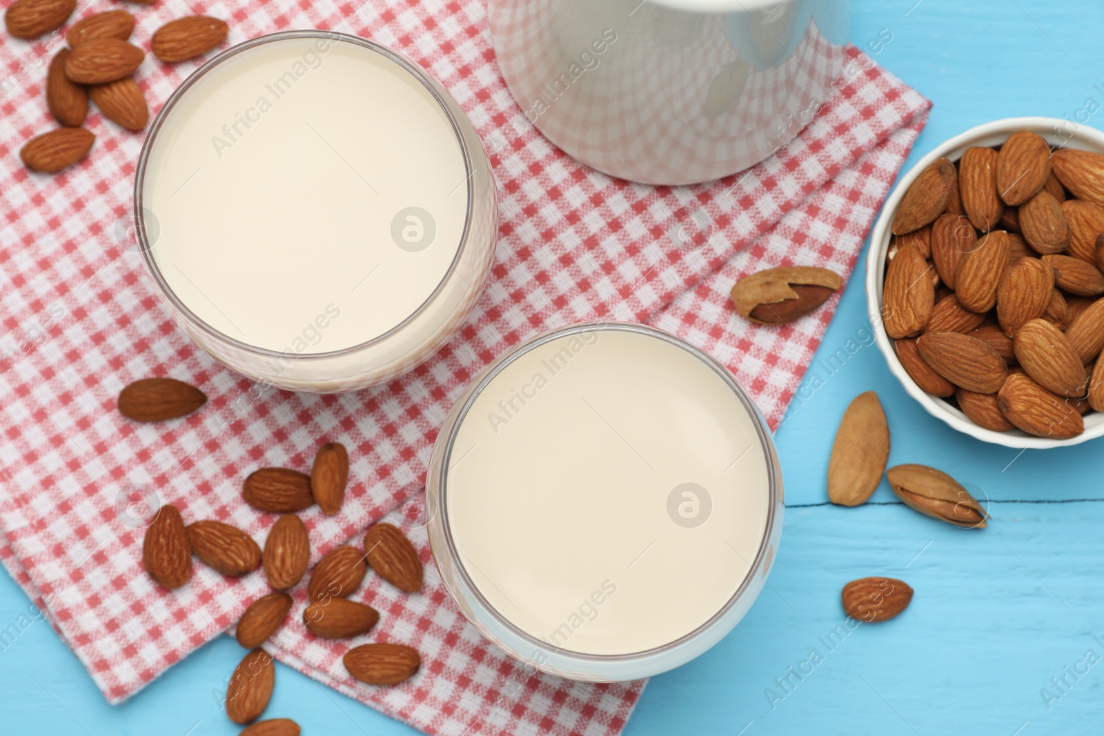 Photo of Fresh nut milk and almonds on light blue wooden table, flat lay