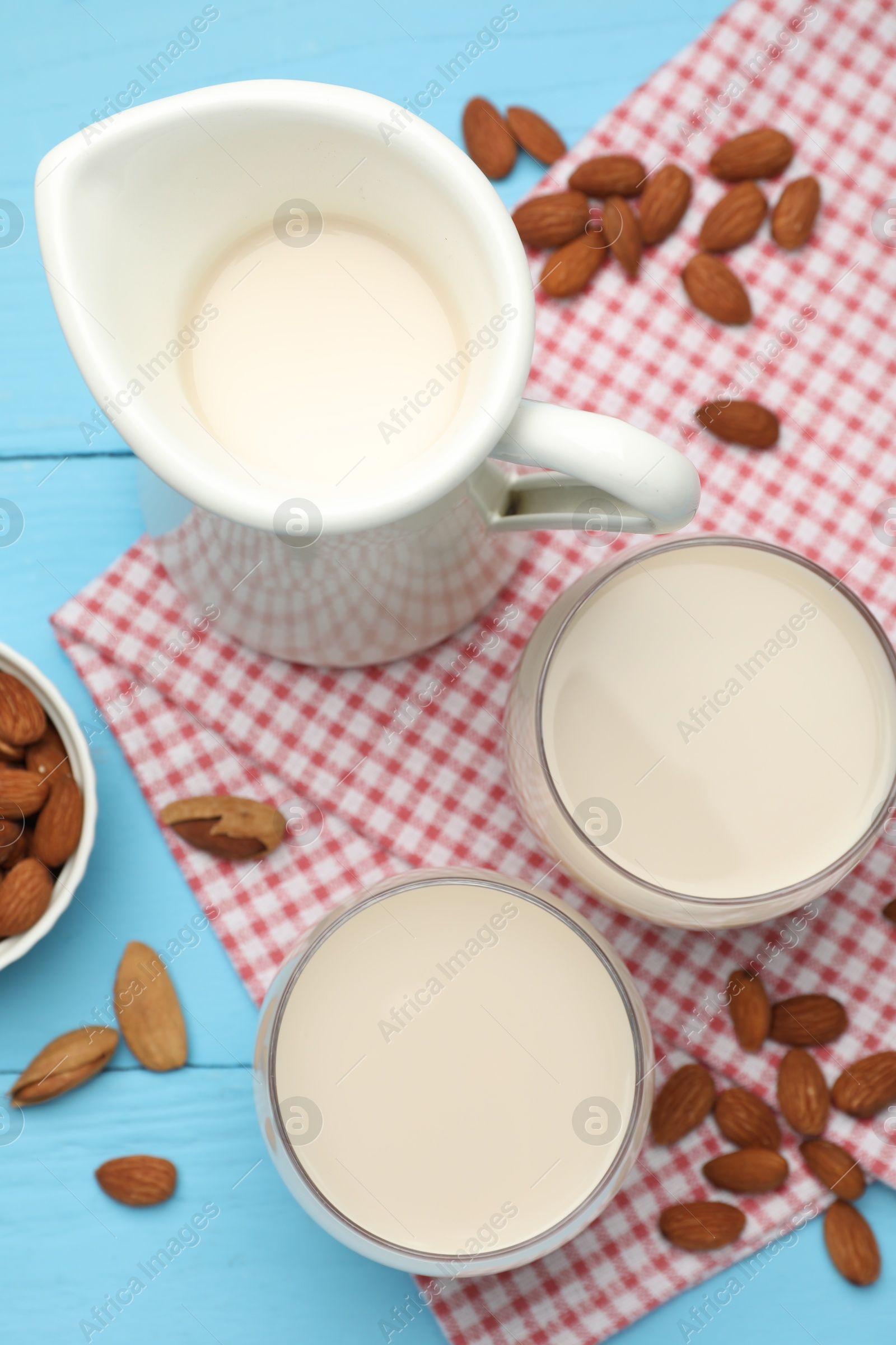 Photo of Fresh nut milk and almonds on light blue wooden table, flat lay