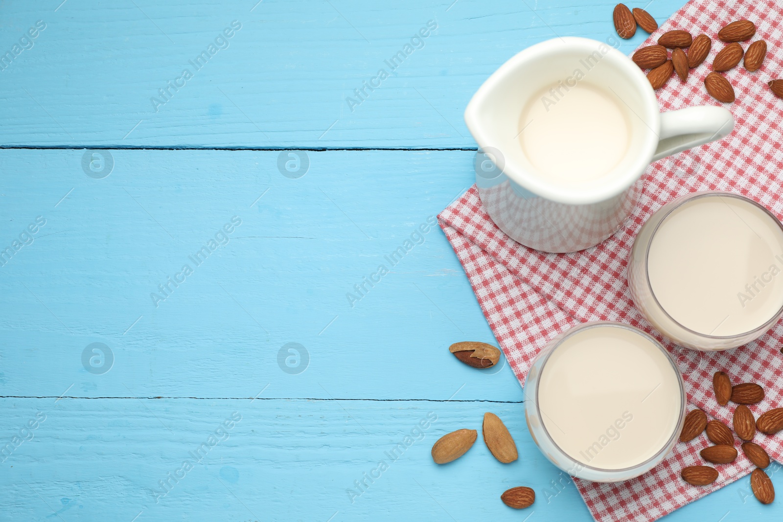 Photo of Fresh nut milk and almonds on light blue wooden table, flat lay. Space for text