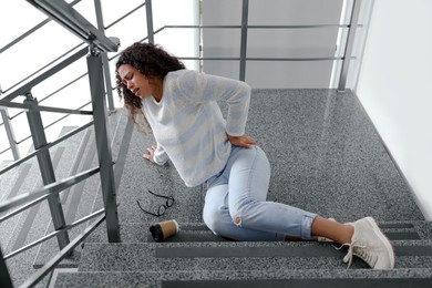 Photo of Woman with injured back on stairs in building after fall. Dangerous accident