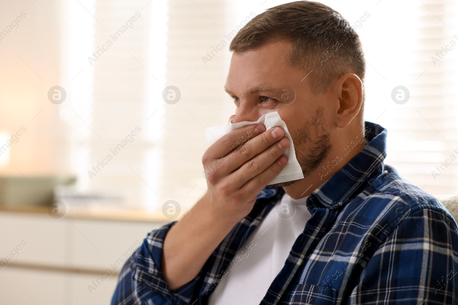 Photo of Man with tissue blowing runny nose at home. Space for text