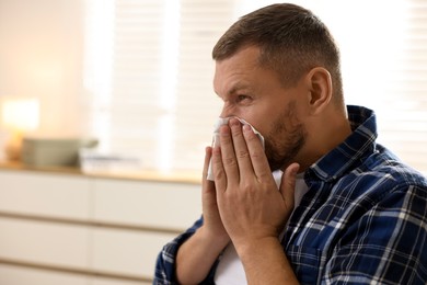 Man with tissue blowing runny nose at home. Space for text