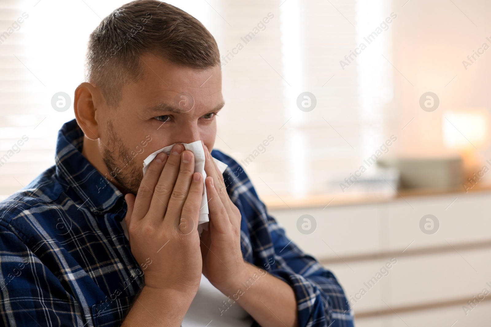 Photo of Man with tissue blowing runny nose at home. Space for text