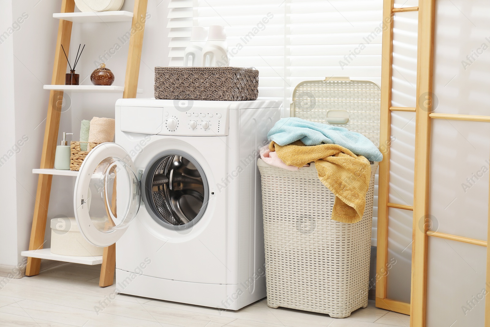 Photo of Wicker basket full of laundry, washing machine and detergents in bathroom