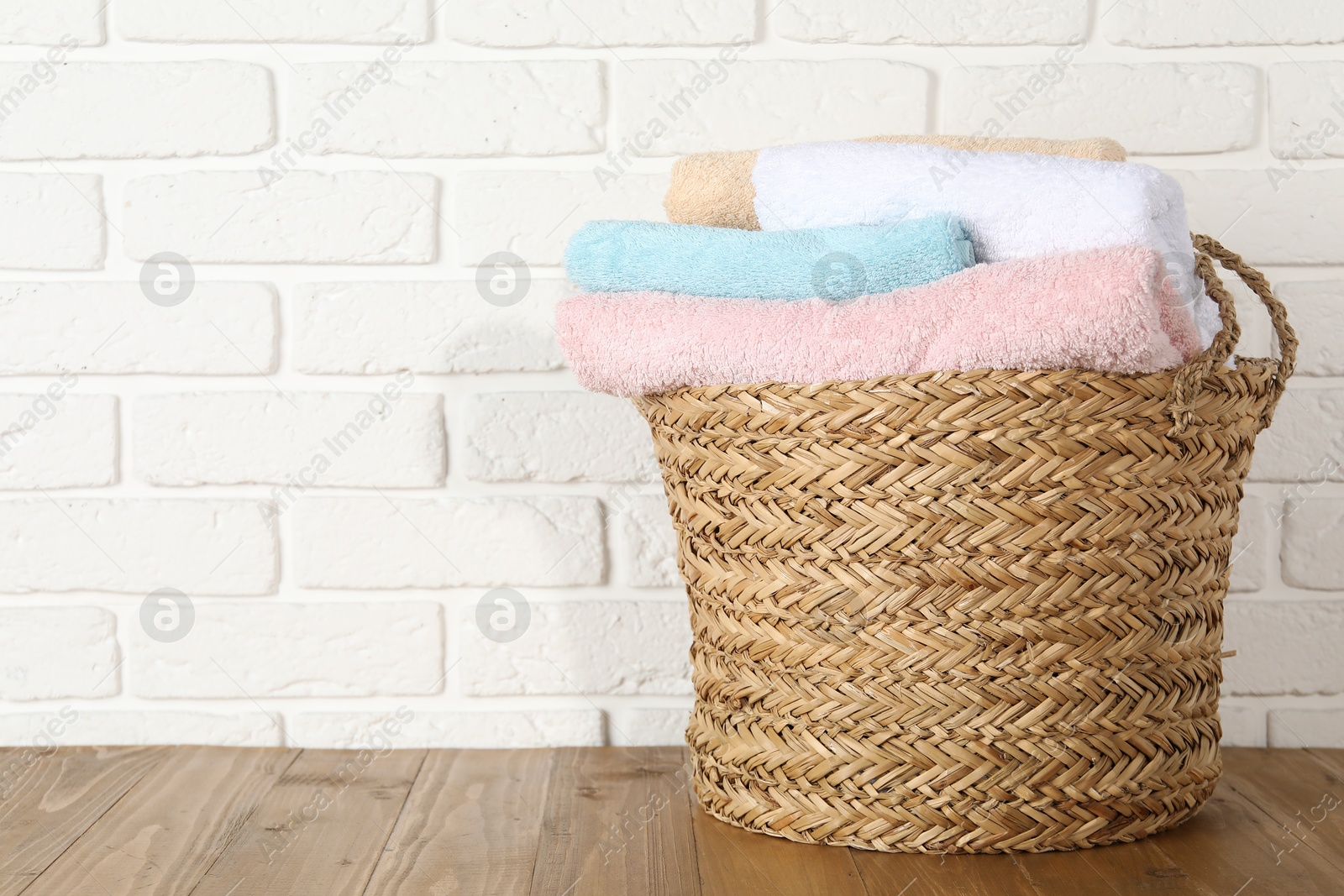 Photo of Wicker basket full of laundry on wooden table, space for text