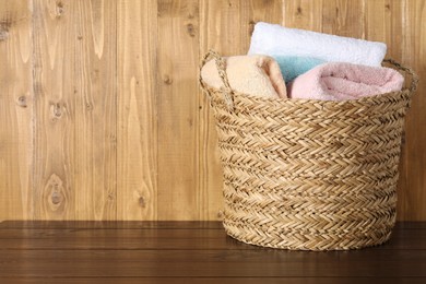 Photo of Wicker basket full of laundry on wooden table, space for text