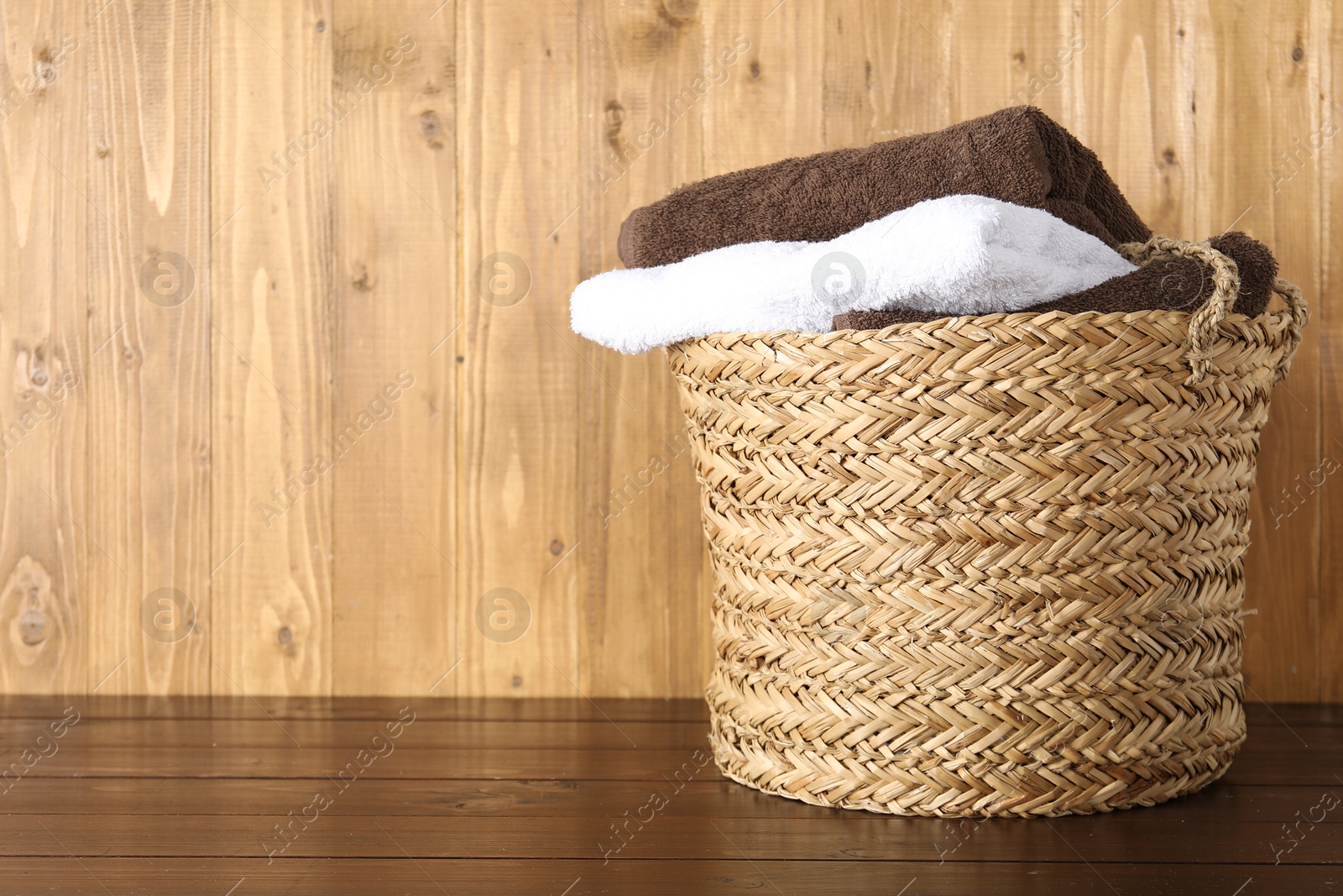 Photo of Wicker basket full of laundry on wooden table, space for text