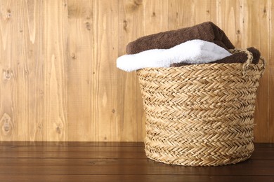 Photo of Wicker basket full of laundry on wooden table, space for text