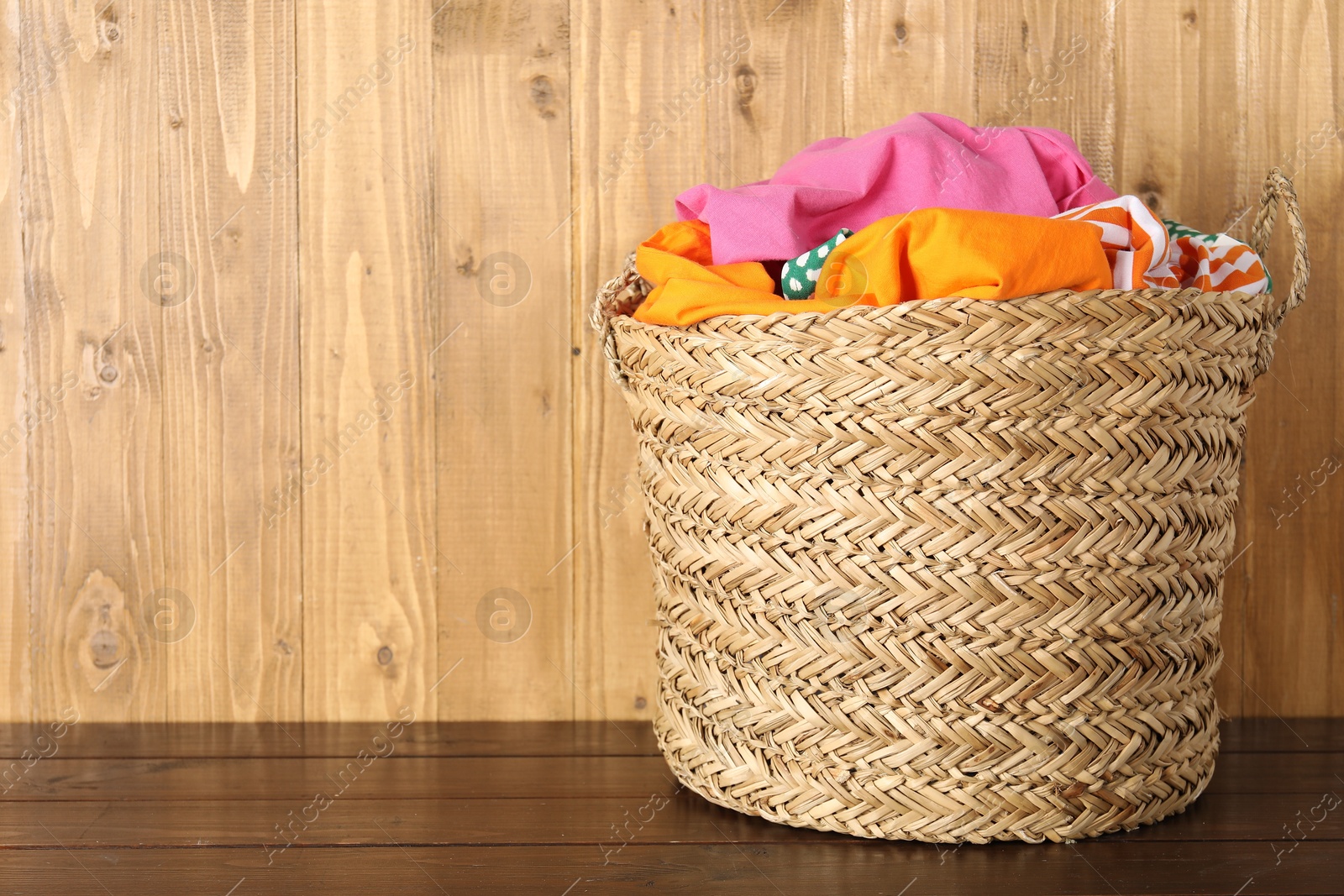 Photo of Wicker basket full of laundry on wooden table, space for text