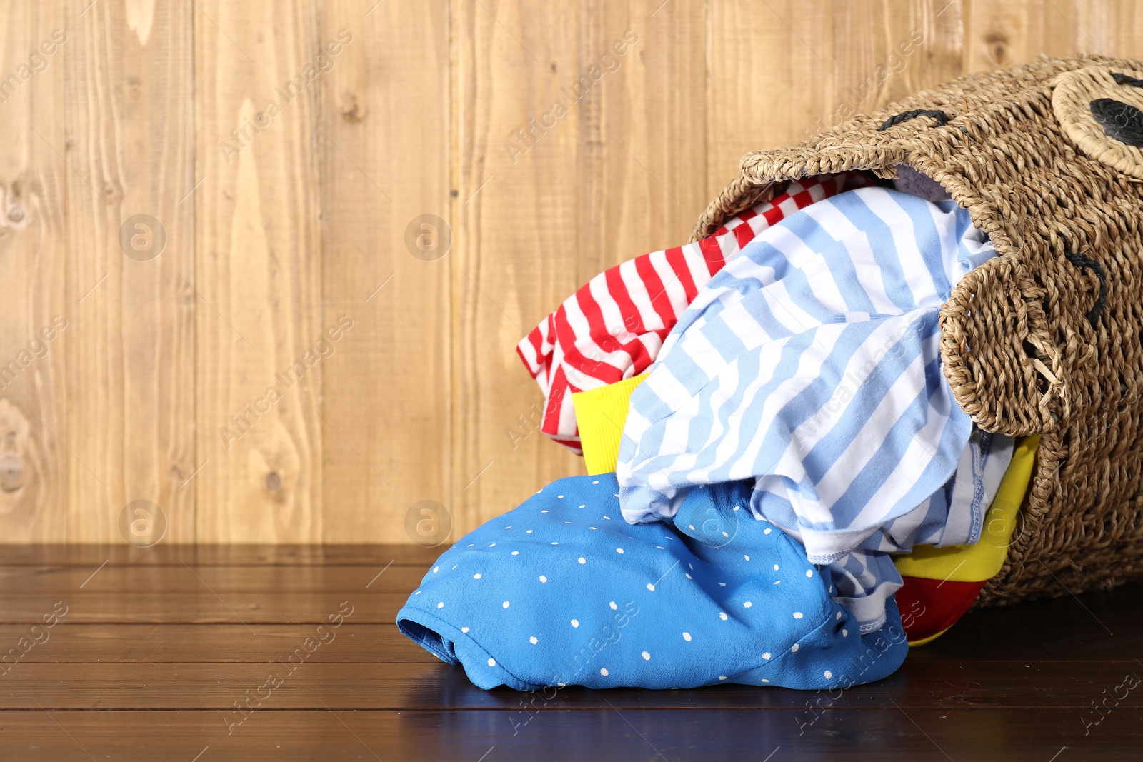 Photo of Overturned wicker basket with laundry on wooden table, space for text