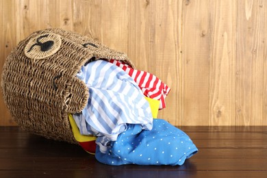 Photo of Overturned wicker basket with laundry on wooden table, space for text