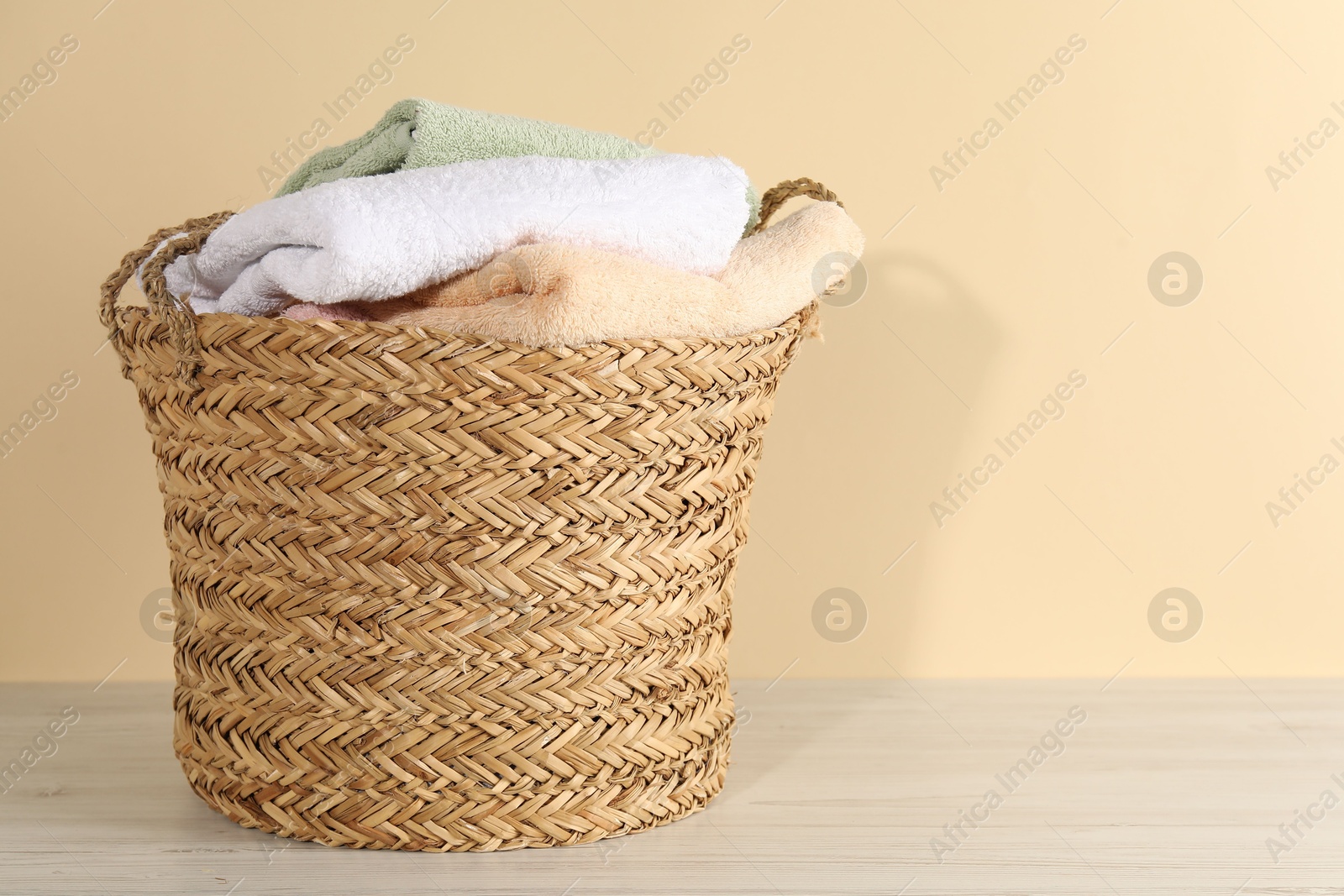 Photo of Wicker basket full of laundry on wooden table against beige background, space for text