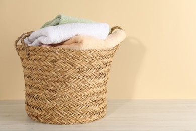 Photo of Wicker basket full of laundry on wooden table against beige background, space for text