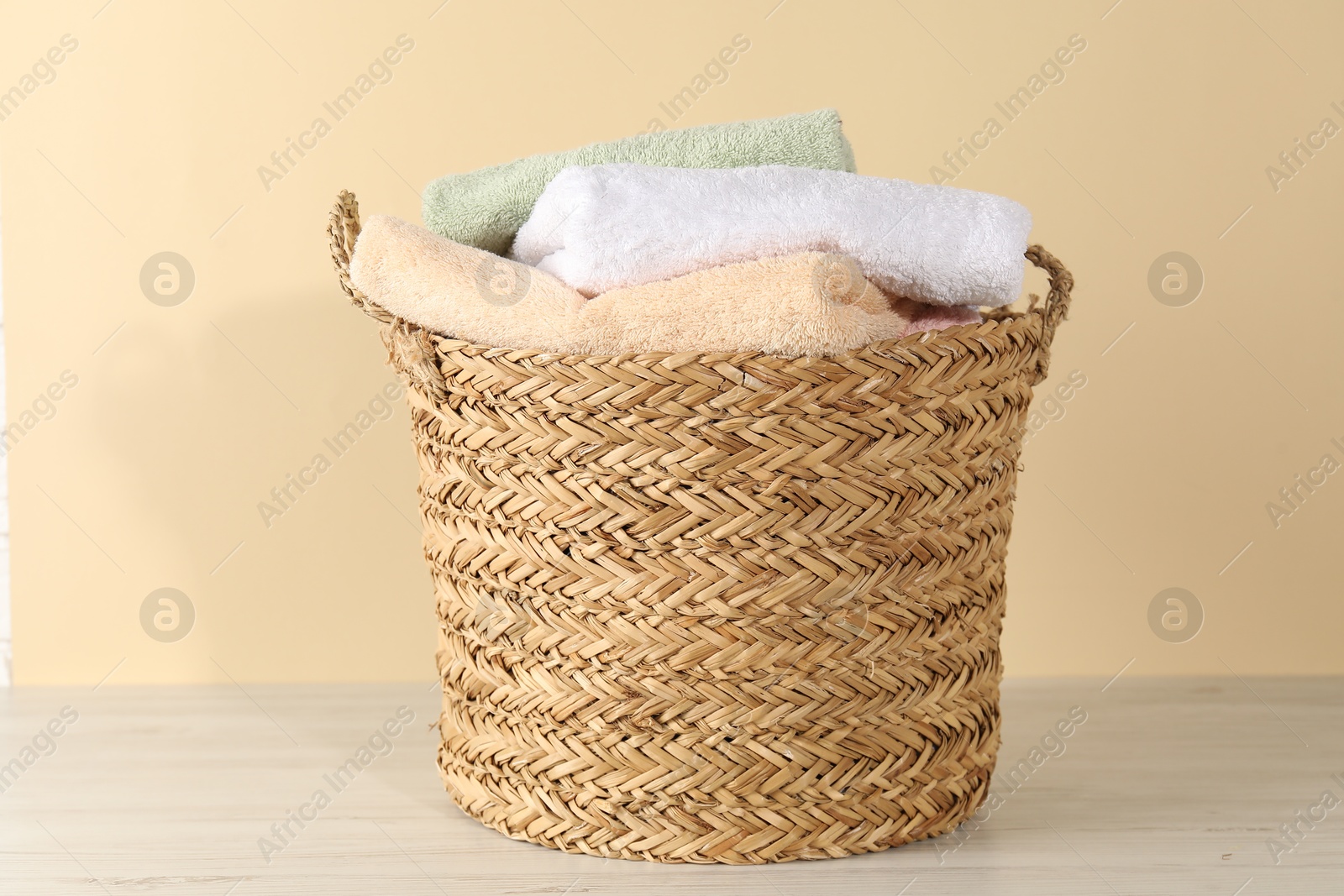 Photo of Wicker basket full of laundry on wooden table against beige background