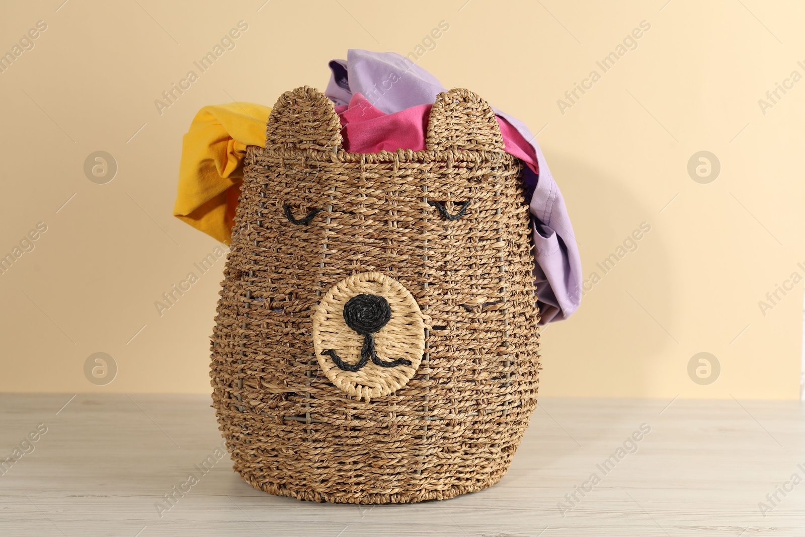 Photo of Wicker basket full of laundry on wooden table against beige background