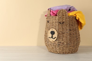 Photo of Wicker basket full of laundry on wooden table against beige background, space for text