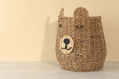 Photo of One wicker laundry basket on wooden table against beige background, space for text