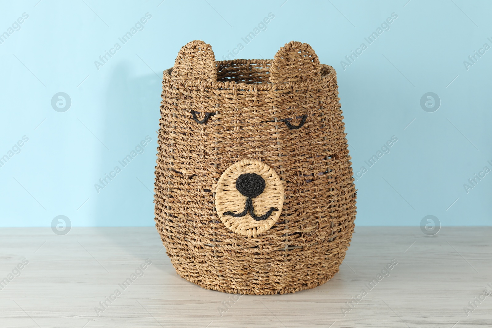 Photo of One wicker laundry basket on wooden table against light blue background