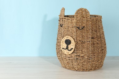 Photo of One wicker laundry basket on wooden table against light blue background, space for text