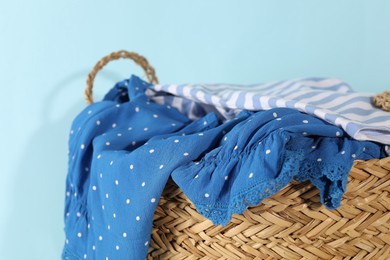 Photo of Wicker basket full of laundry on light blue background, closeup