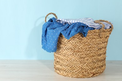 Photo of Wicker basket full of laundry on wooden table against light blue background, space for text