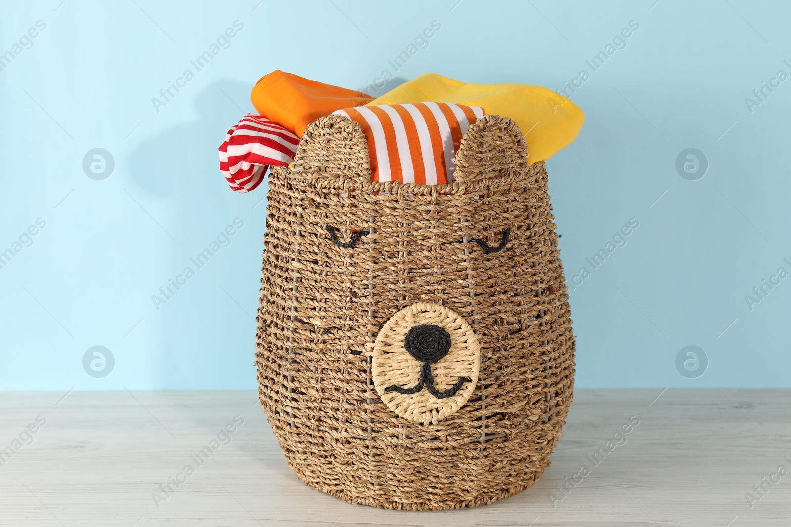 Photo of Wicker basket full of laundry on wooden table against light blue background