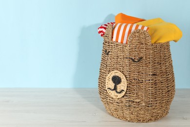 Photo of Wicker basket full of laundry on wooden table against light blue background, space for text