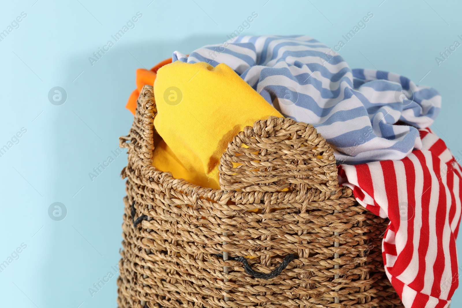 Photo of Wicker basket full of laundry on light blue background, closeup