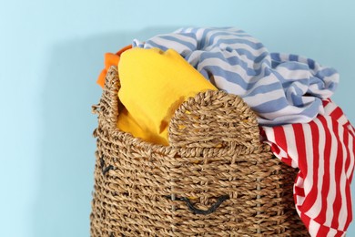 Photo of Wicker basket full of laundry on light blue background, closeup