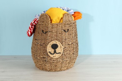 Photo of Wicker basket full of laundry on wooden table against light blue background