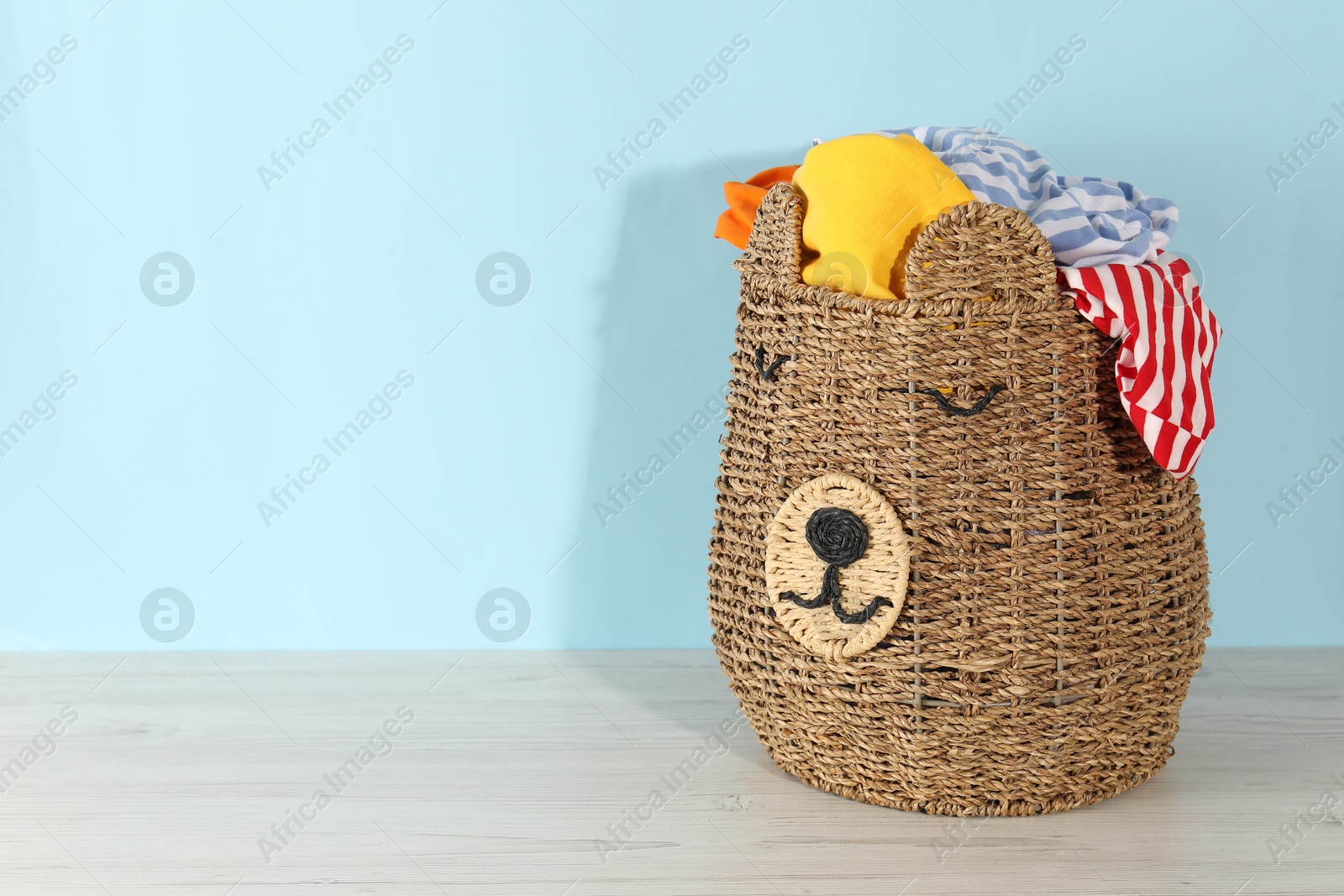 Photo of Wicker basket full of laundry on wooden table against light blue background, space for text