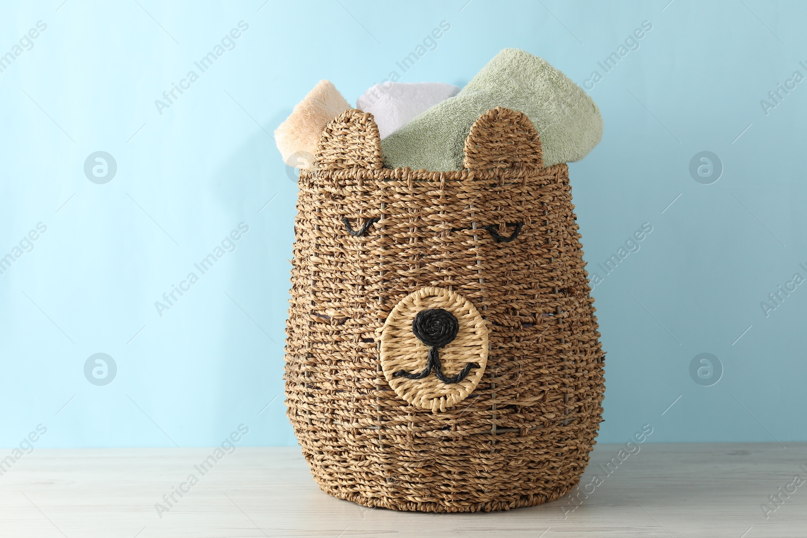 Photo of Wicker basket full of laundry on wooden table against light blue background