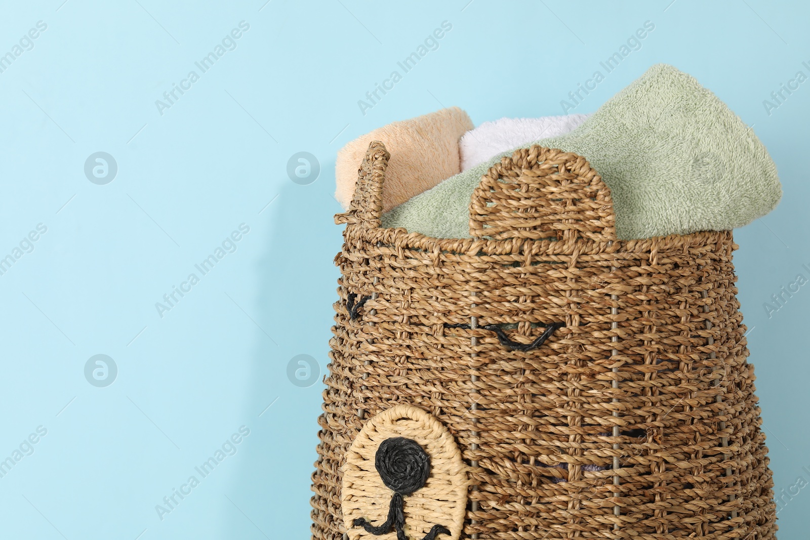 Photo of Wicker basket full of laundry on light blue background, closeup. Space for text