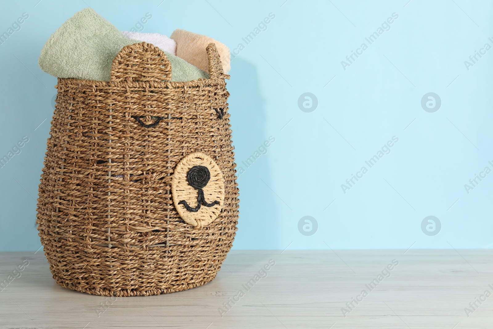 Photo of Wicker basket full of laundry on wooden table against light blue background, space for text