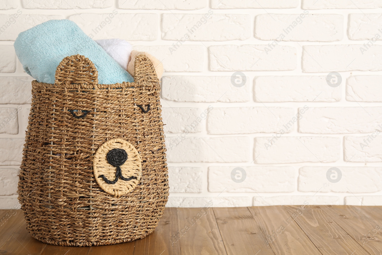 Photo of Wicker basket full of laundry on wooden table, space for text