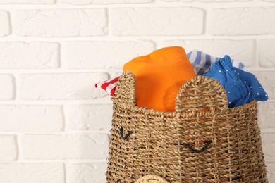 Photo of Wicker basket full of laundry near white brick wall, closeup. Space for text