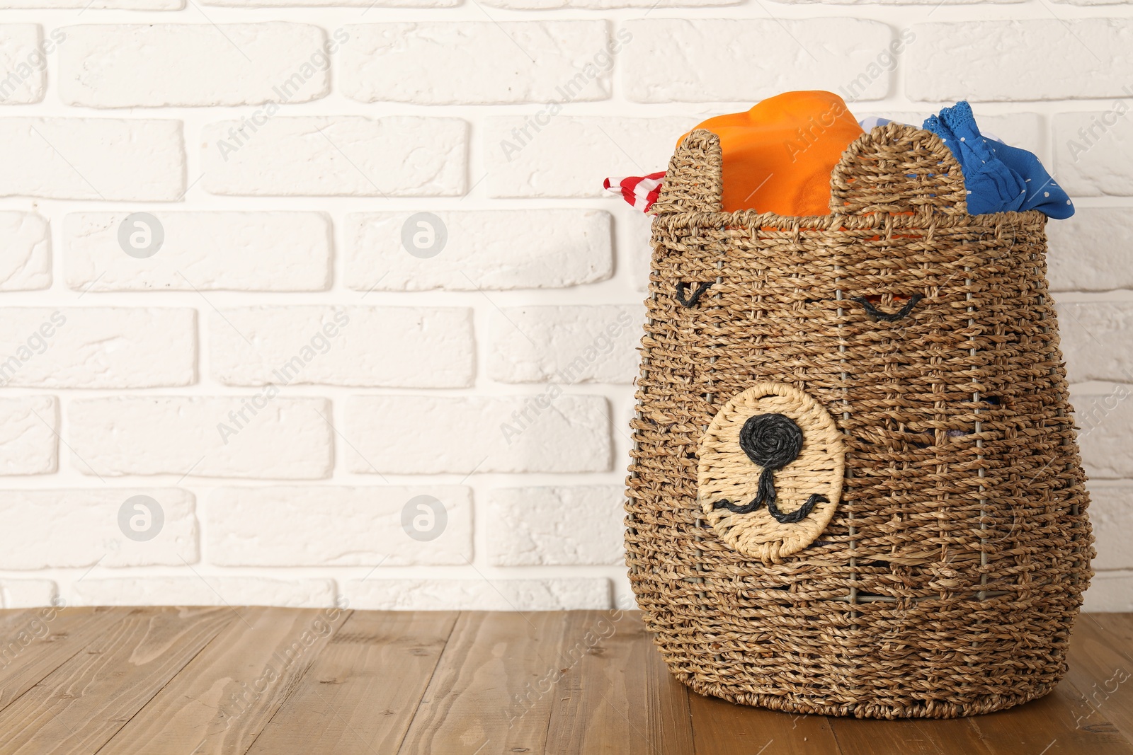 Photo of Wicker basket full of laundry on wooden table, space for text