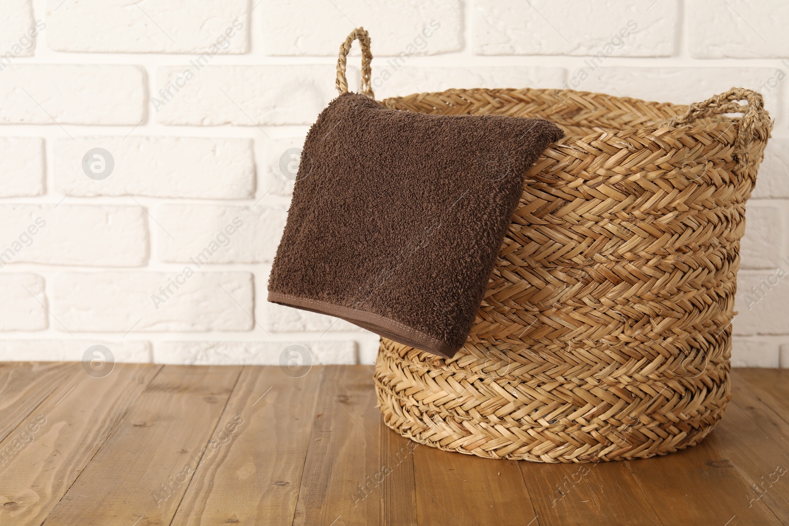 Photo of Wicker laundry basket with towel on wooden table, space for text