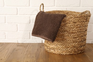 Photo of Wicker laundry basket with towel on wooden table, space for text