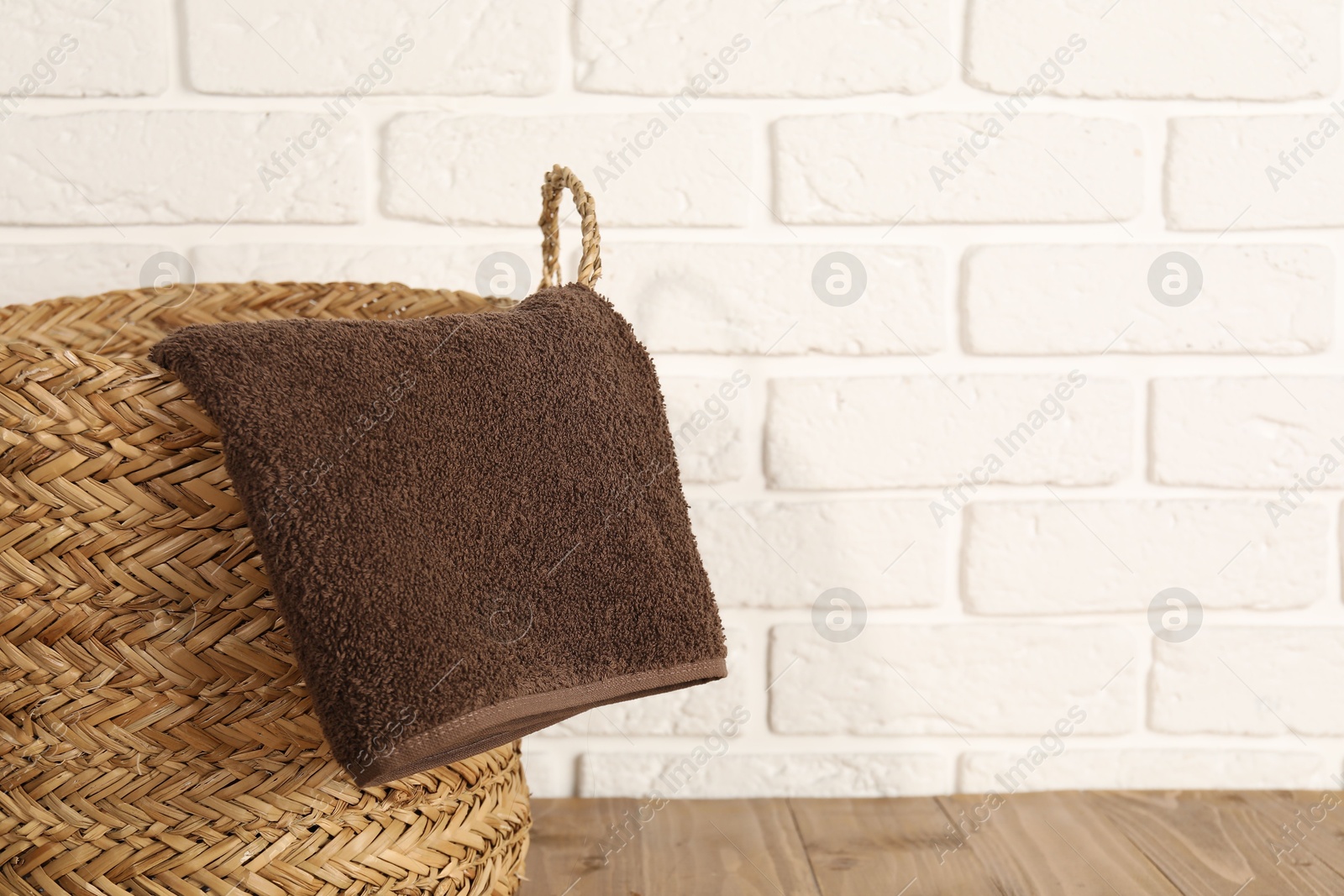 Photo of Wicker laundry basket with towel on wooden table, closeup. Space for text