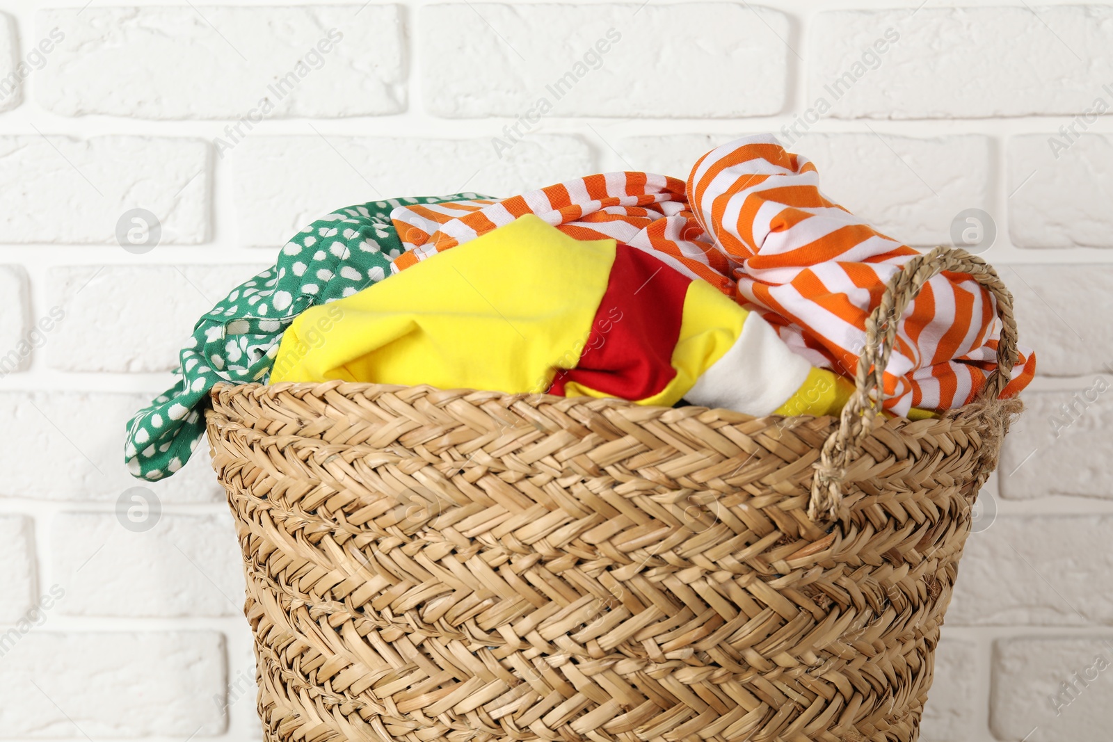 Photo of Wicker basket full of laundry near white brick wall, closeup