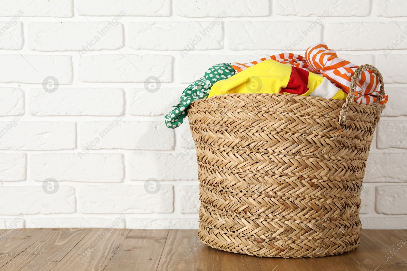 Photo of Wicker basket full of laundry on wooden table, space for text