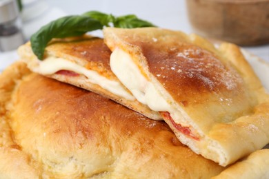 Photo of Pieces of delicious calzone pizza with mozzarella, tomatoes and basil on table, closeup