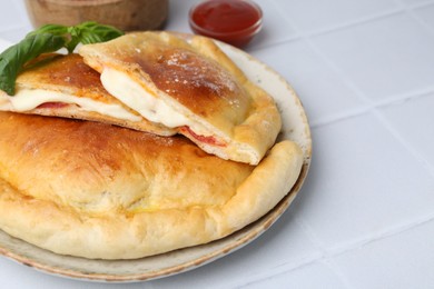 Photo of Pieces of delicious calzone pizza with mozzarella, tomatoes and basil on white tiled table, closeup