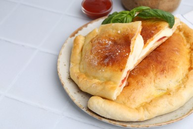 Photo of Pieces of delicious calzone pizza with mozzarella, tomatoes and basil on white tiled table, closeup