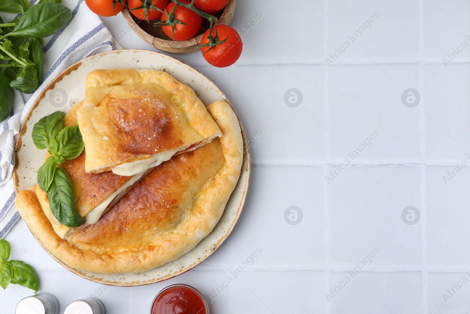 Photo of Pieces of delicious calzone pizza with mozzarella, tomatoes and basil on white tiled table, flat lay. Space for text