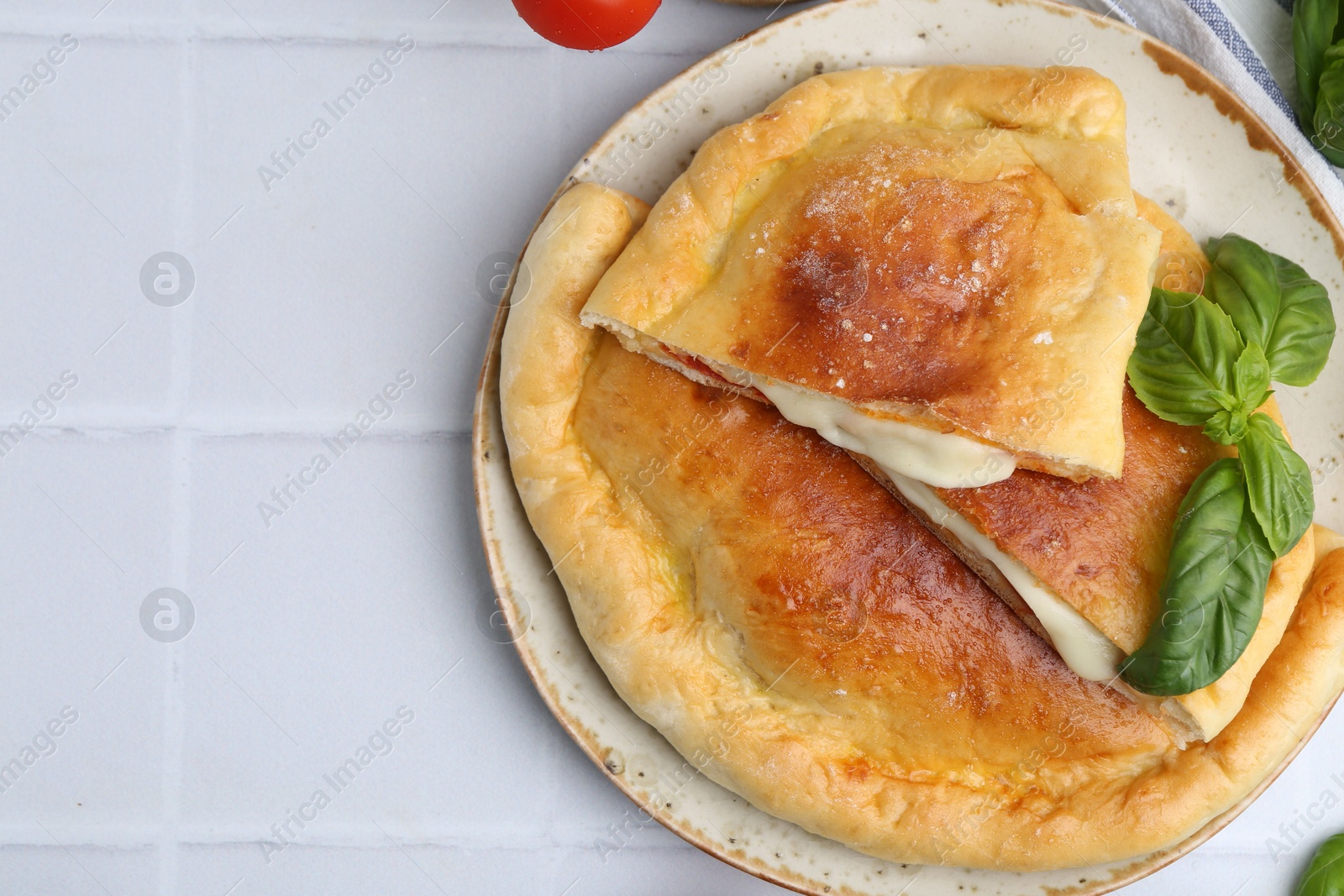 Photo of Pieces of delicious calzone pizza with mozzarella, tomatoes and basil on white tiled table, top view. Space for text